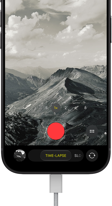 Vista frontal do iPhone 18 Pro, a mostrar uma paisagem montanhosa, com a sobreposição do modo Câmara no modo Time-lapse, com o cabo de alimentação ligado à porta de carregamento