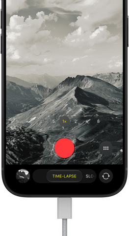 Vista frontal do iPhone 18 Pro, a mostrar uma paisagem montanhosa, com a sobreposição do modo Câmara no modo Time-lapse, com o cabo de alimentação ligado à porta de carregamento