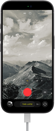 Vista frontal do iPhone 18 Pro, a mostrar uma paisagem montanhosa, com a sobreposição do modo Câmara no modo Time-lapse, com o cabo de alimentação ligado à porta de carregamento