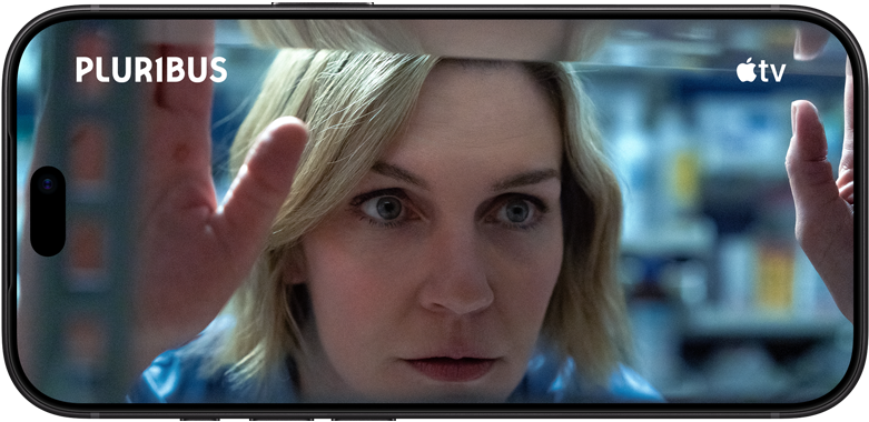 iPhone 18 Pro, colocado na horizontal, a mostrar um grande plano de uma mulher a olhar para fora da janela. Título da série: Pluribus